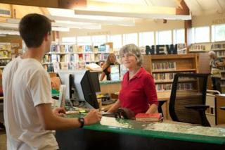 Lady helping a person check out books at the circulation desk. 